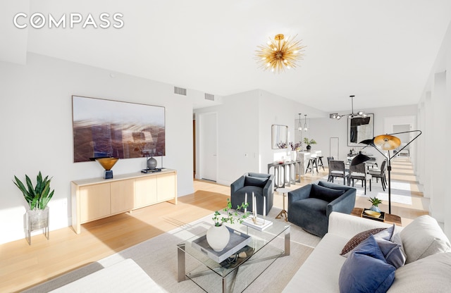 living room featuring stairs, a notable chandelier, visible vents, and light wood-style floors