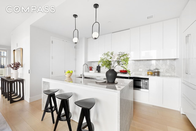 kitchen with a breakfast bar, a sink, light wood-style flooring, backsplash, and pendant lighting