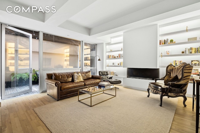 living room with a tray ceiling, a wall of windows, and light wood-style floors