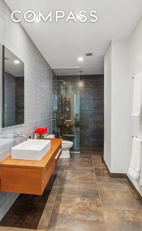 bathroom featuring visible vents, toilet, vanity, a walk in shower, and tile walls