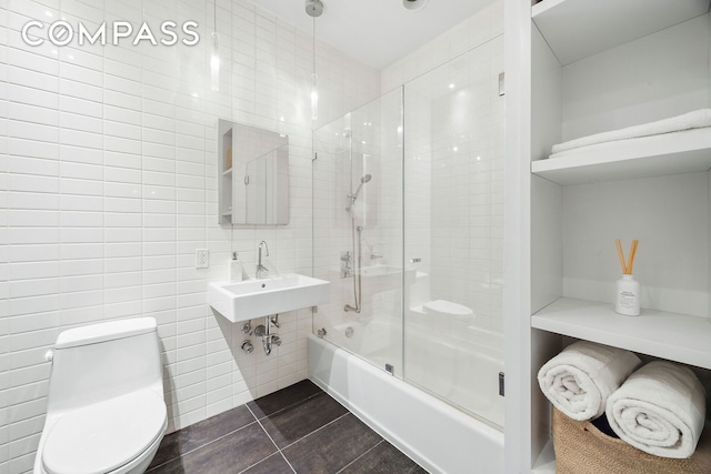 bathroom featuring tile walls, toilet, combined bath / shower with glass door, a sink, and tile patterned floors