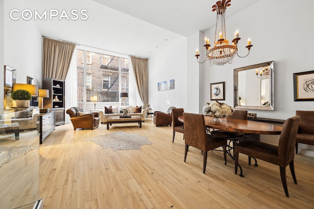 dining area featuring light wood-type flooring, a towering ceiling, and an inviting chandelier