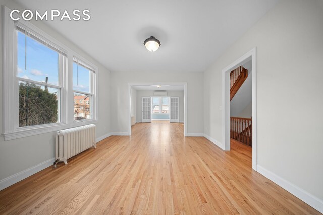 empty room with baseboards, light wood-style floors, a wall mounted AC, and radiator