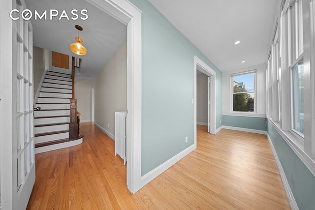 corridor with radiator, light wood-style floors, stairs, and baseboards