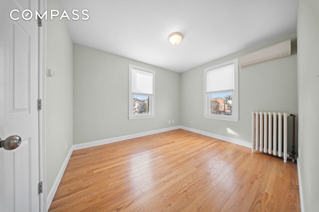 unfurnished room with an AC wall unit, baseboards, light wood finished floors, and radiator heating unit