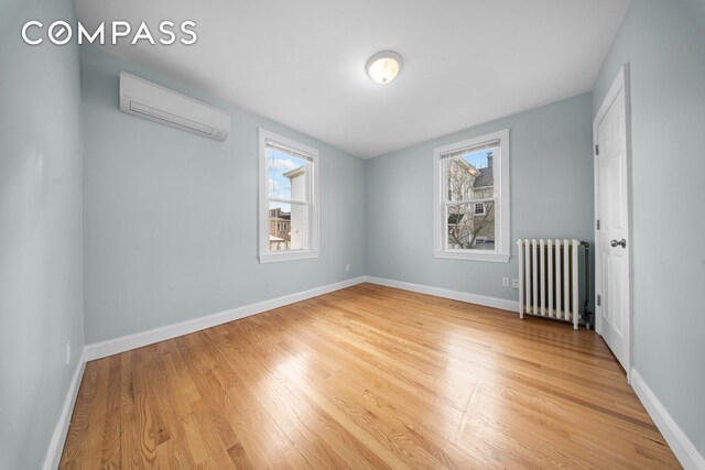 unfurnished room with light wood finished floors, radiator heating unit, a wall mounted air conditioner, and baseboards