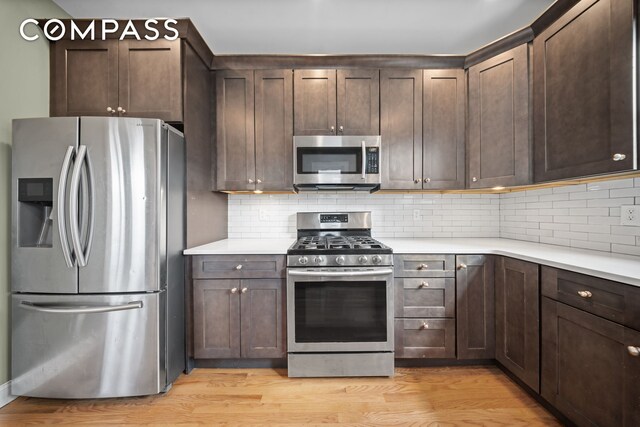 kitchen with appliances with stainless steel finishes, light wood-type flooring, dark brown cabinetry, and tasteful backsplash