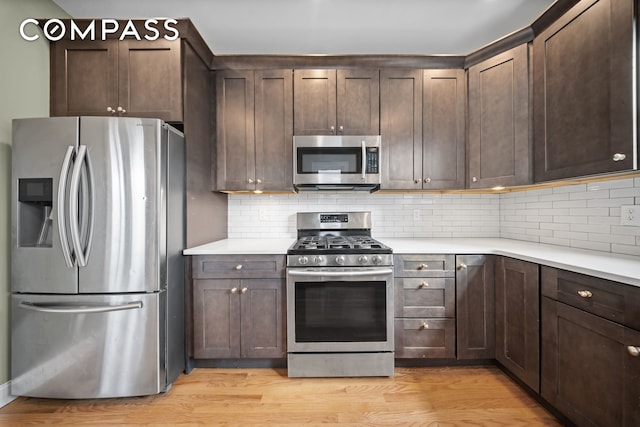 kitchen with dark brown cabinetry, decorative backsplash, stainless steel appliances, and light wood-type flooring