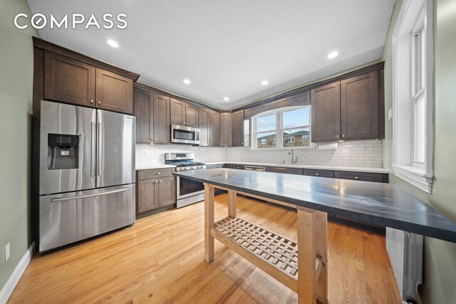 kitchen featuring appliances with stainless steel finishes, light wood-type flooring, a sink, and dark brown cabinets