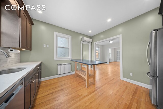 kitchen featuring stainless steel appliances, a sink, an AC wall unit, decorative backsplash, and radiator