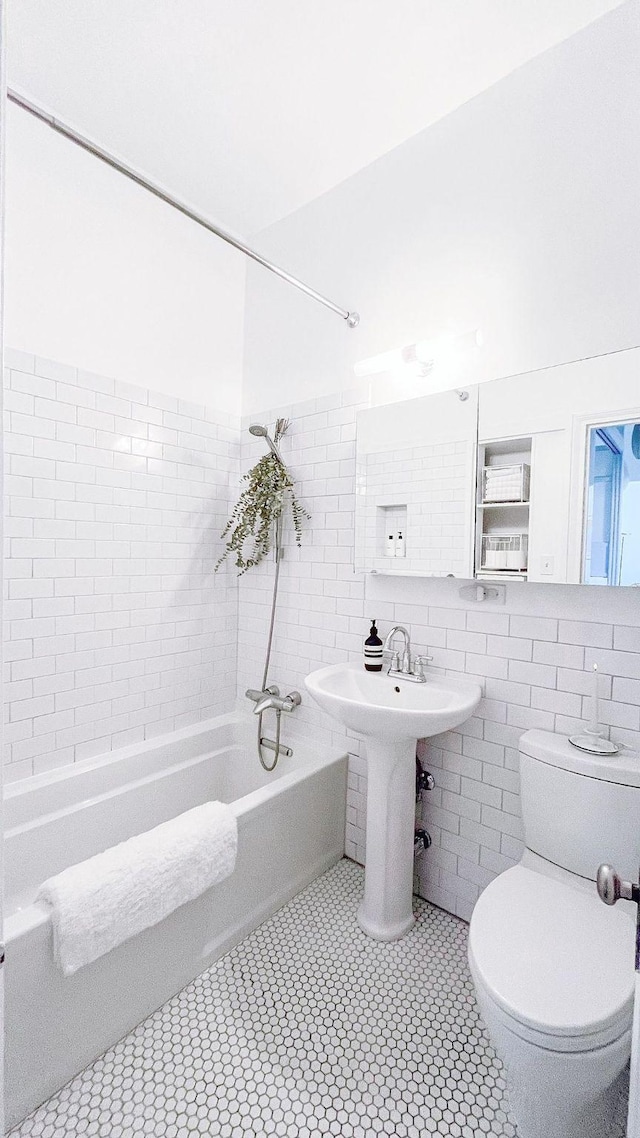 full bath featuring toilet, a sink, bathing tub / shower combination, tile walls, and tile patterned floors