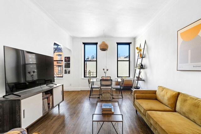 living area with dark wood-style floors, arched walkways, and baseboards