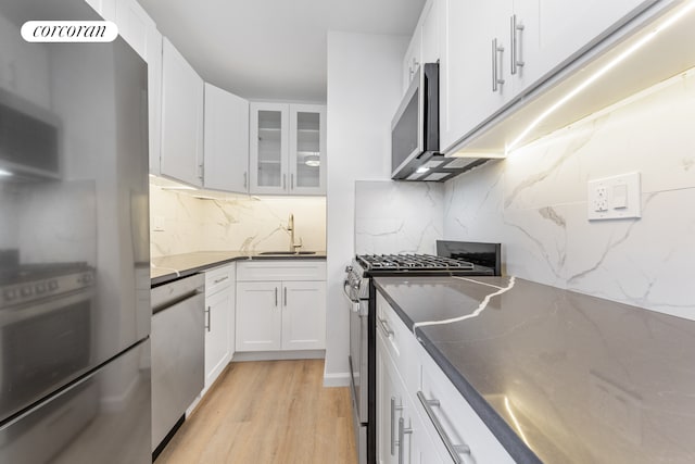 kitchen with dark countertops, glass insert cabinets, stainless steel appliances, white cabinetry, and a sink