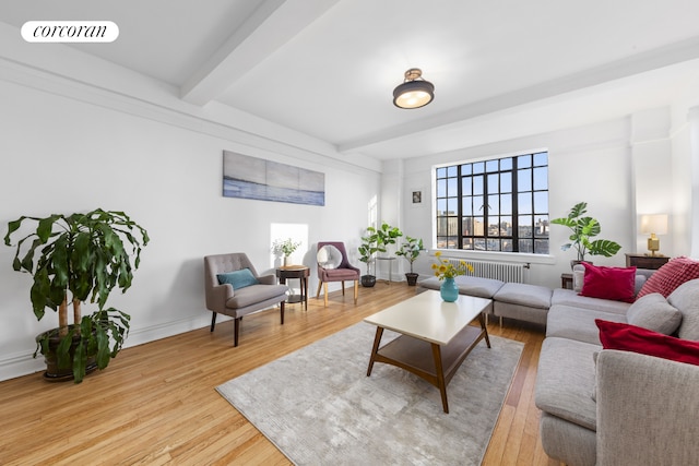 living room featuring light wood-style flooring, visible vents, baseboards, beamed ceiling, and radiator heating unit