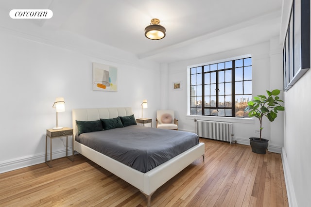 bedroom with beam ceiling, radiator, visible vents, light wood-style floors, and baseboards