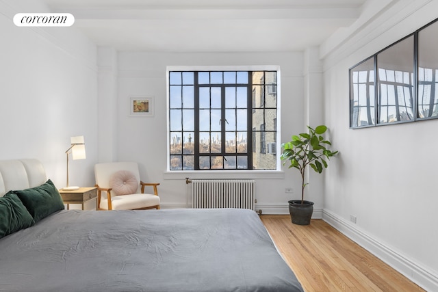 bedroom featuring baseboards, visible vents, radiator heating unit, and wood finished floors