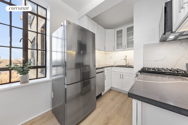 kitchen featuring stainless steel appliances, a sink, white cabinetry, dark countertops, and glass insert cabinets