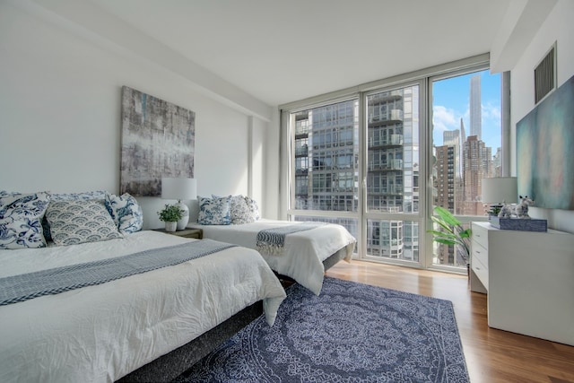 bedroom with a view of city, a wall of windows, and wood finished floors