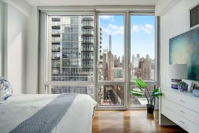 bedroom with multiple windows, wood finished floors, visible vents, and a city view