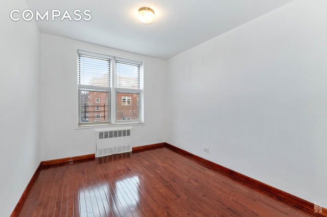 spare room featuring dark wood-type flooring, radiator, and baseboards