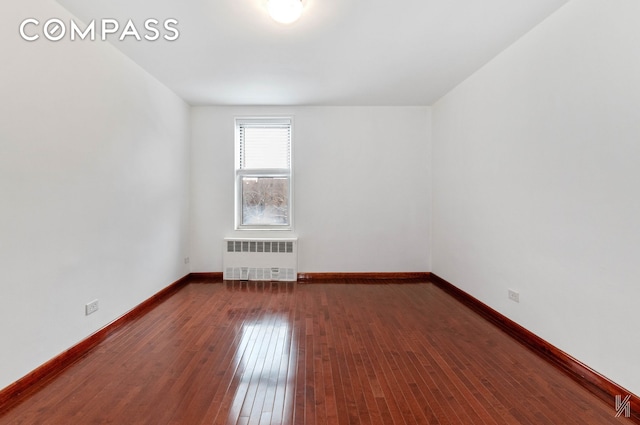 spare room featuring radiator, baseboards, and dark wood-style flooring