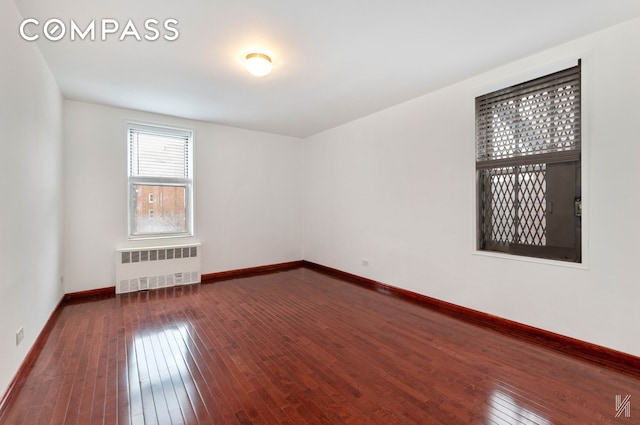 unfurnished room with dark wood-type flooring, baseboards, and radiator heating unit