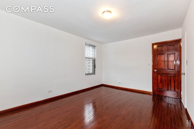 unfurnished room featuring baseboards and dark wood-type flooring