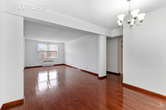 empty room with a notable chandelier, dark wood-type flooring, baseboards, and radiator