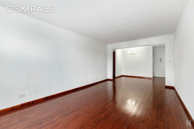 spare room with wood-type flooring, baseboards, and a notable chandelier