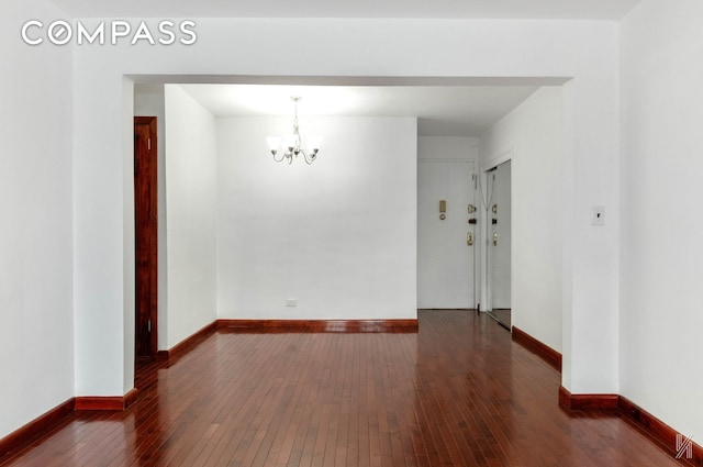 empty room featuring an inviting chandelier, dark wood finished floors, and baseboards