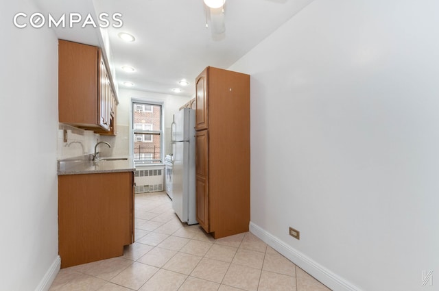 kitchen featuring brown cabinets, a sink, freestanding refrigerator, and decorative backsplash