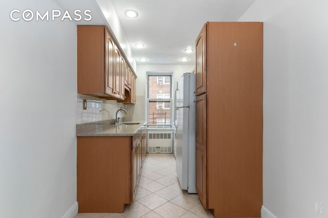 kitchen featuring light tile patterned floors, decorative backsplash, radiator, freestanding refrigerator, and a sink