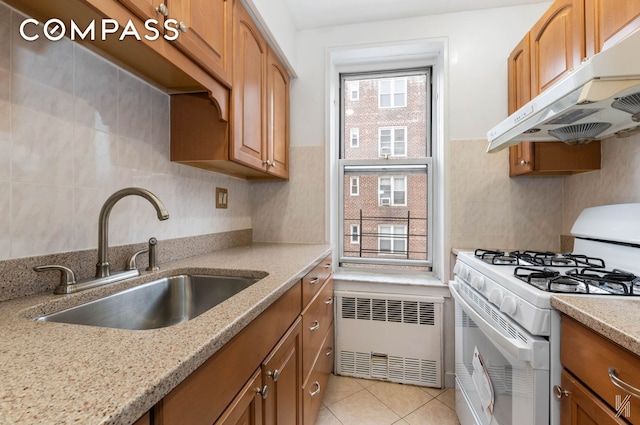 kitchen featuring light stone counters, radiator heating unit, a sink, under cabinet range hood, and white gas range oven