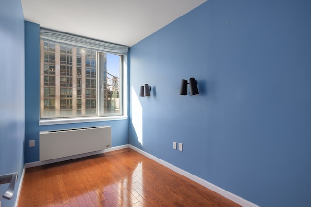 unfurnished room with hardwood / wood-style flooring, baseboards, and radiator