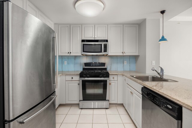 kitchen featuring light tile patterned floors, stainless steel appliances, hanging light fixtures, a sink, and light stone counters