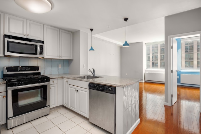 kitchen with a peninsula, light stone countertops, stainless steel appliances, white cabinetry, and a sink