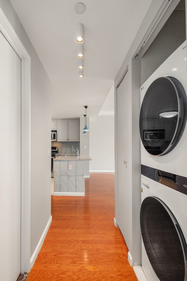 laundry area with stacked washer and dryer, baseboards, laundry area, and light wood-type flooring