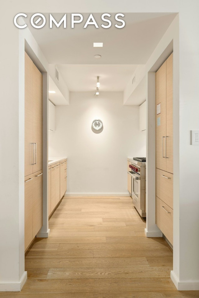 kitchen with modern cabinets, light brown cabinetry, light wood-style floors, stainless steel stove, and baseboards