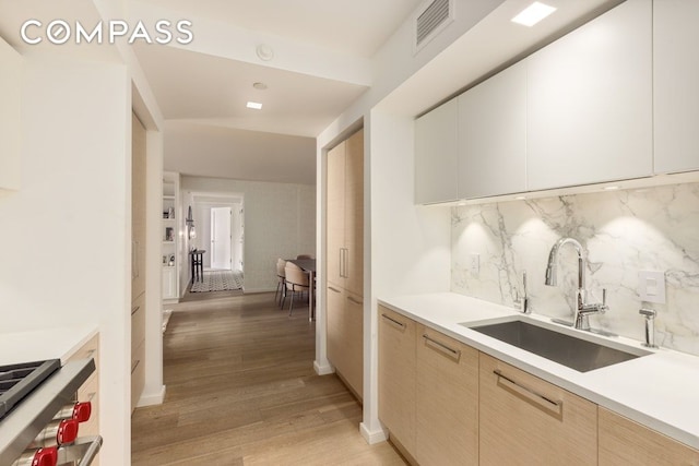 kitchen with a sink, light countertops, decorative backsplash, modern cabinets, and light wood-style flooring