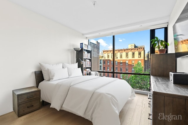 bedroom with light wood-style flooring, a view of city, and a wall of windows