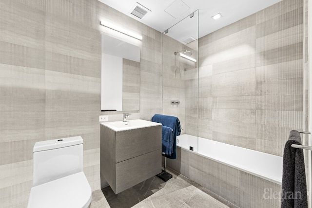 bathroom featuring visible vents, toilet, tiled shower / bath combo, vanity, and tile walls