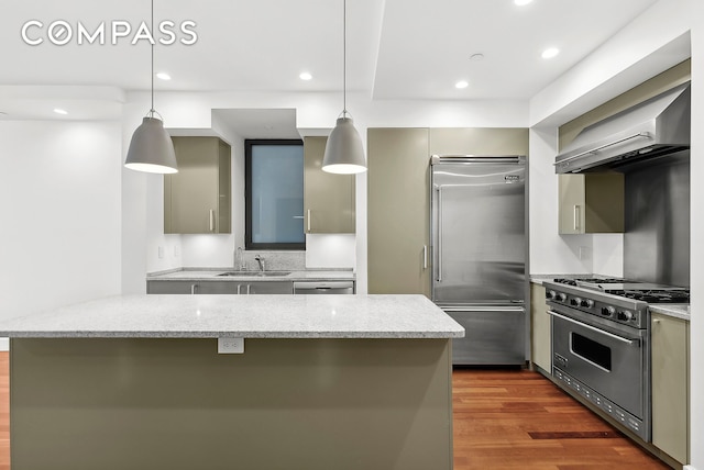 kitchen featuring a sink, light stone countertops, wall chimney exhaust hood, high end appliances, and decorative light fixtures