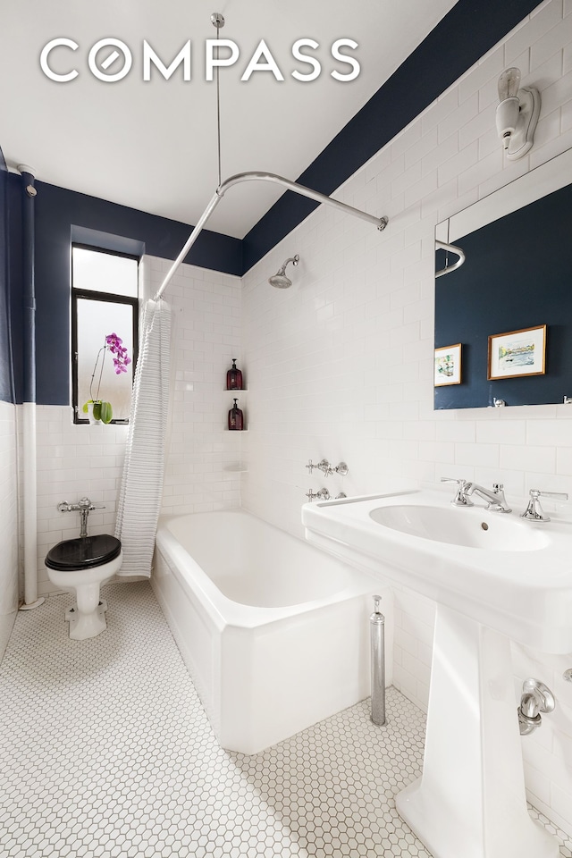 full bath featuring tile patterned floors, tile walls, shower / bath combo with shower curtain, and a sink