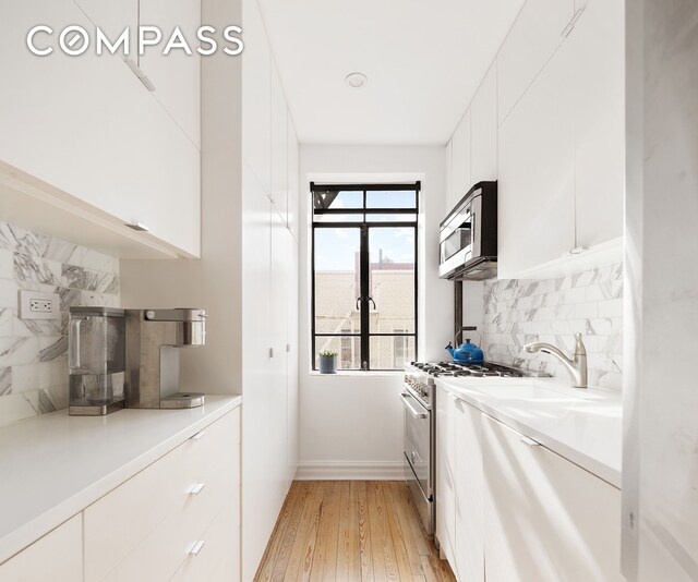 kitchen featuring decorative backsplash, modern cabinets, appliances with stainless steel finishes, light wood-type flooring, and white cabinetry