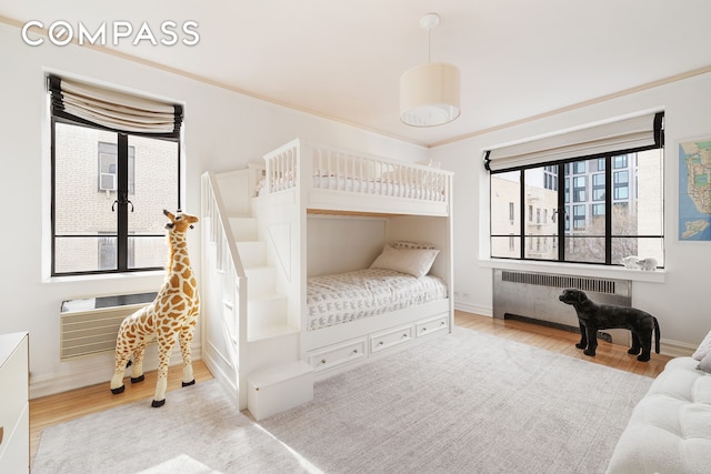 bedroom featuring baseboards, radiator, wood finished floors, and a wall unit AC