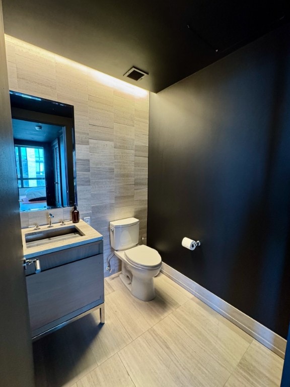 half bath with visible vents, toilet, vanity, tile patterned flooring, and baseboards