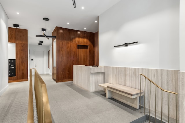 hallway with an upstairs landing, recessed lighting, light colored carpet, and wainscoting