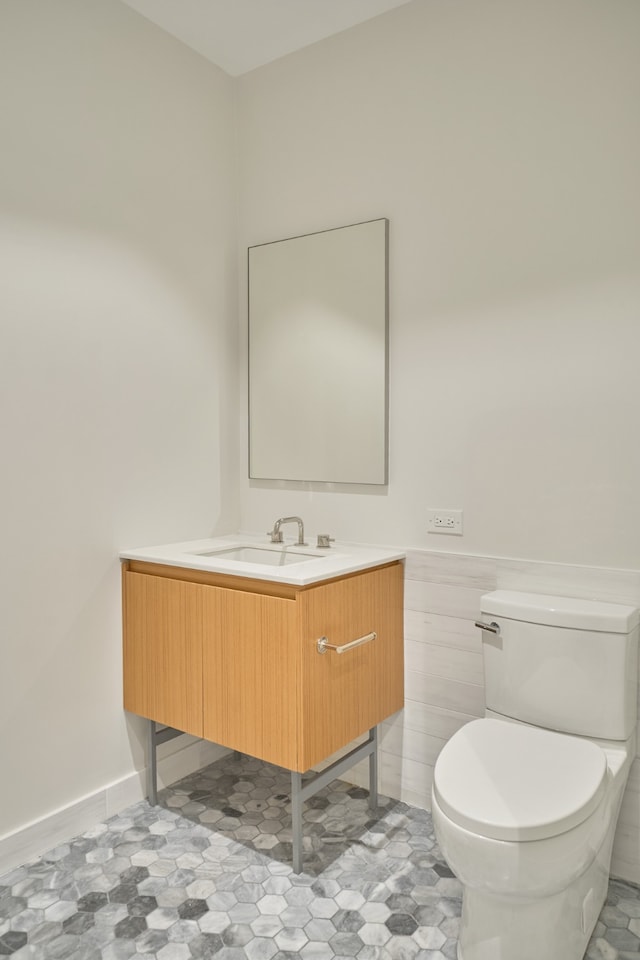 half bathroom with toilet, wainscoting, and vanity