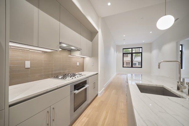 kitchen with light wood finished floors, extractor fan, decorative backsplash, appliances with stainless steel finishes, and a sink