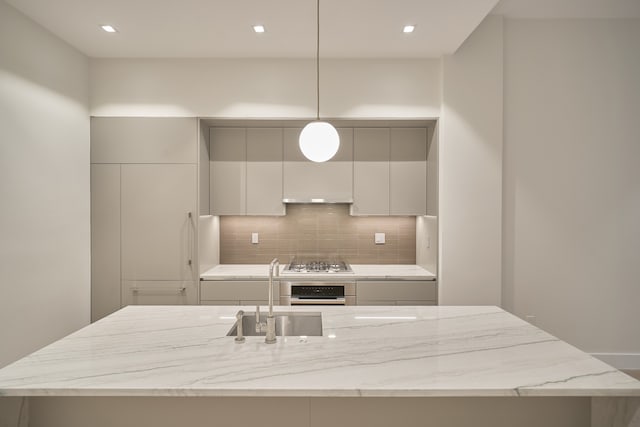 kitchen featuring light stone counters, a center island with sink, stainless steel appliances, a sink, and backsplash